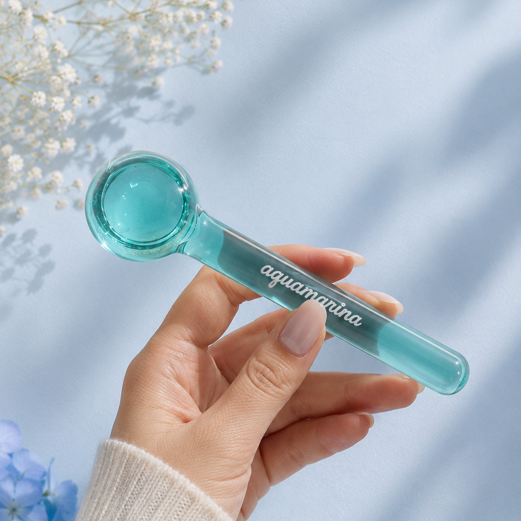 Hand holding a teal-colored tool with 'aquamarina' branding against a light blue background with flowers.
